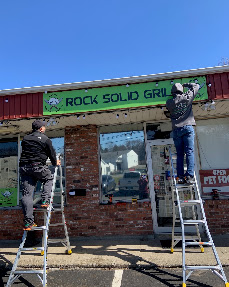 Rock Solid Grill storefront sign being installed above the shop